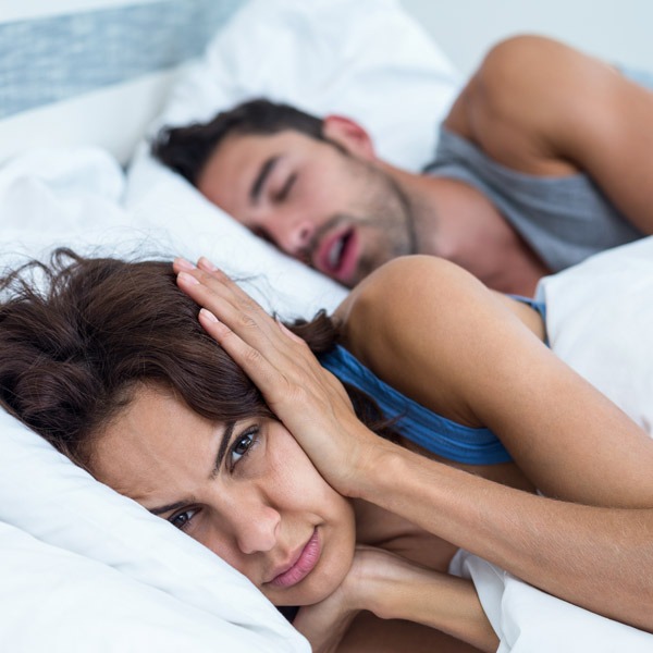 woman covering ears while man snores