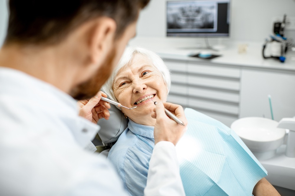 Elderly woman in a dental chair smiling at the denturist during a denture exam.