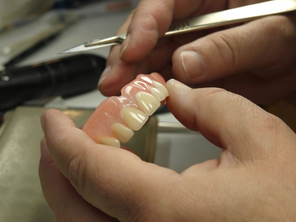 Denturist working on upper mouth dentures while holding a scalpel.
