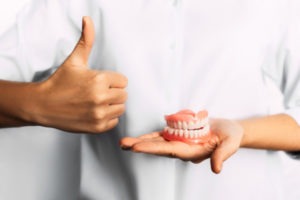 denturist holding pair of dentures in hand with thumbs up