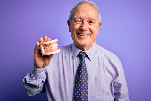 man smiling and holding dentures