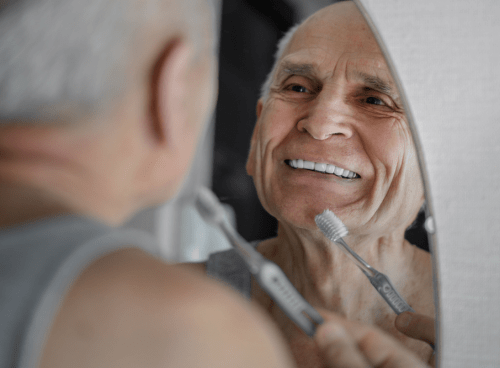 man brushing his dentures in front of a mirror